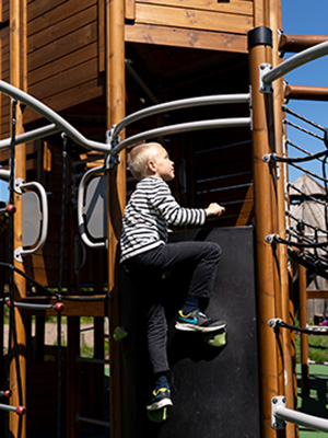 A boy climbs up onto a wooden playground unit.